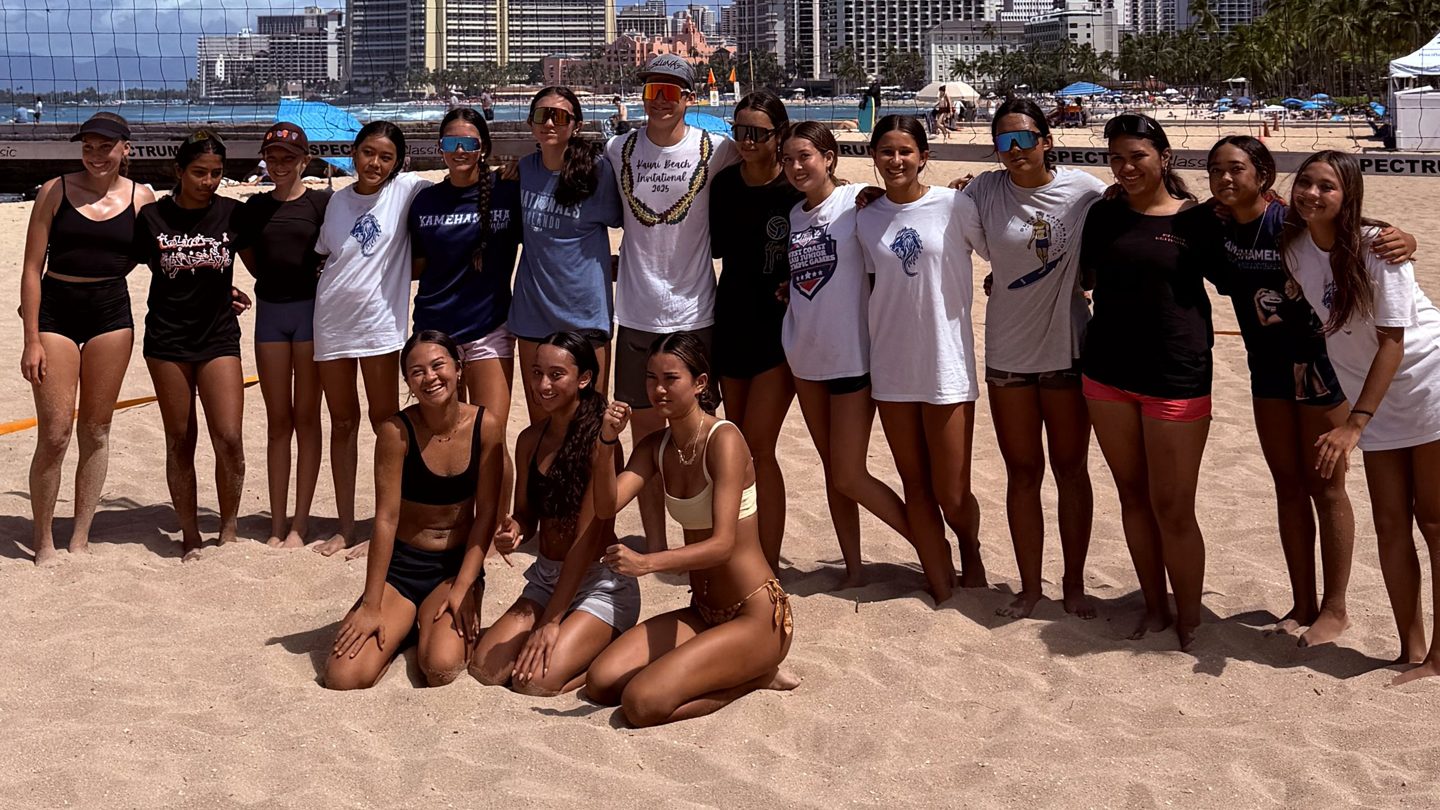 Beach volleyball players posing together beside a court net on the sand, with hotels and the ocean behind them